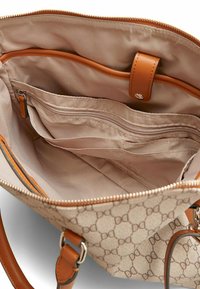 Beige håndtaske med en tan-farvet, mønstret yderside. Indvendigt har den en glat, lys tan-foring, flere lommer og en metal lynlås.