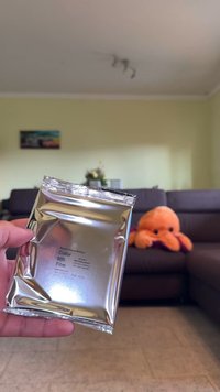 Ασημένια συσκευασία ταινίας 600, με την επιγραφή "Roving Frames Edition", με κείμενο και λεπτομέρειες, κρατημένη σε ένα χέρι; μαλακή πορτοκαλί πλαστική καρκινοειδής φιγούρα στο φόντο.