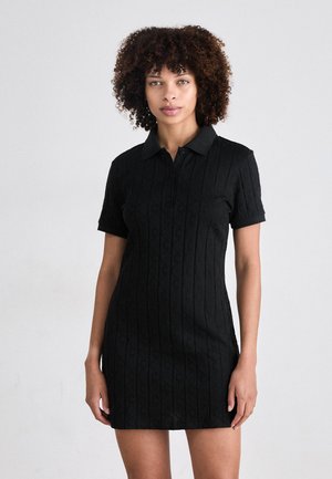 Abito polo nero con maniche corte, caratterizzato da un motivo testurizzato, un colletto e una chiusura a bottoni. Design slim fit.