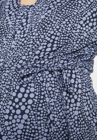 Mekko merisotilastyyli, jossa on vaaleansiniset pyöreät pilkut. Kangas on pehmeä tekstuuri ja vyötäröllä on solmittava yksityiskohta.