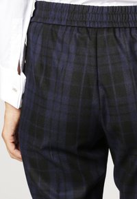 Granatowe spodnie w kratę wykonane z miękkiego materiału, z elastycznym pasem i luźnym krojem. Szczegóły obejmują gładką fakturę i subtelny połysk.