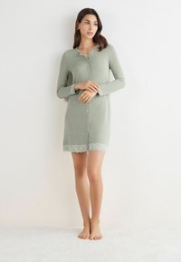 Světlý zelený noční úbor s dlouhými rukávy, knoflíkovým zapínáním vpředu a krajkovým lemem na spodní části a rukávech. Měkká tkanina s hladkou texturou.