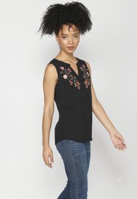 Blusa nera senza maniche con scollatura a V e ricami floreali in rosa e verde lungo la parte frontale. Bottoni al centro, tessuto morbido.