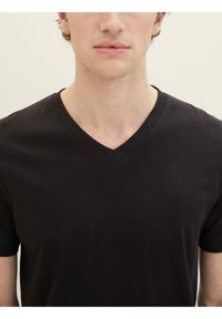 Tricou negru cu decolteu în V, realizat dintr-un material de bumbac fin, cu mâneci scurte și un detaliu de cusătură subtil la guler.