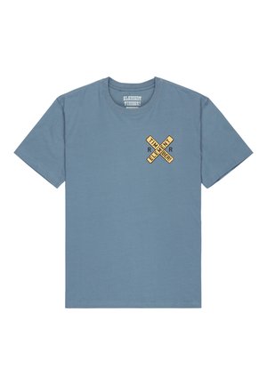 Valkoinen lyhythihainen puuvillapaita vaaleansinisessä sävyssä ja pyöreällä kaula-aukolla. Rinnassa on graafinen suunnittelu, jossa on ristikkäisiä keltaisia elementtejä.