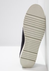 Semelle de chaussure de sport en daim noir avec une semelle extérieure en caoutchouc blanc texturé. Présente des rainures horizontales et la taille "37" moulée sur le côté.