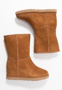 Par de botas de ante marrón de media caña con suelas de goma ligeras en color beige, mostradas lado a lado sobre un fondo blanco.