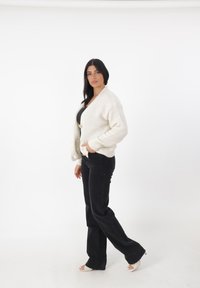 Ivoor gebreide cardigan met een V-hals en lange mouwen, voorzien van een knoopsluiting; gecombineerd met zwarte flared jeans en open teen schoenen.
