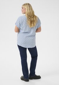 Camicia azzurro chiaro con un motivo geometrico, maniche corte, abbinata a jeans blu scuro e scarpe nere; design casual adatto per l'uso quotidiano.