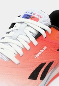 Vieglie Reebok sporta apavi ar sietu augšdaļu, pakāpeniski pārejot no korallkrāsas uz pelēku dizainu, baltām auklām, melniem akcentiem un logo sānos.