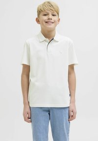 Polo shirt blanc avec un petit logo, doté d'un col contrastant bleu marine. Assorti à un jean en denim bleu clair. Texture en coton lisse.
