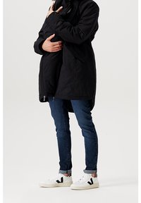 Černá dlouhá bunda na zip s vysokým límcem. Kombinovaná s modrými džíny a bílými teniskami s černými detaily, představující ležérní vzhled.