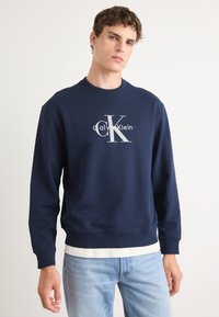 Sweatshirt azul-marinho feito de mistura de algodão, com gola redonda e punhos canelados. Grande logótipo frontal em branco contrastante.