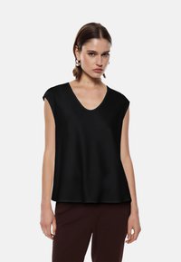 Top senza maniche nero con scollo a V, realizzato in un tessuto lisci. Caratterizzato da una vestibilità rilassata e un orlo leggermente arrotondato.