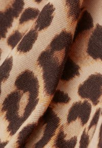 Infoanprint tyg som har en beige bakgrund med mörkbruna och tan fläckar. Texturen är vävd med synliga fibrer.
