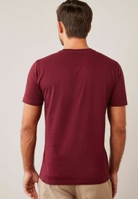 Burgundy puuvillapaita, jossa on pyöreä pääntie, lyhyet hihat ja sileä rakenne; yksinkertainen muotoilu ilman näkyviä kuvioita tai yksityiskohtia.