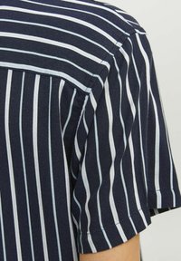 Camisa de manga corta azul marino con finas rayas verticales blancas, cuello con botonadura y diseño en el yugo trasero. Textura de tela suave.