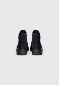 Botas de ante negras hasta el tobillo con un acabado texturizado, tacón cuadrado y cremallera lateral, vistas desde atrás, mostrando un diseño liso y minimalista.