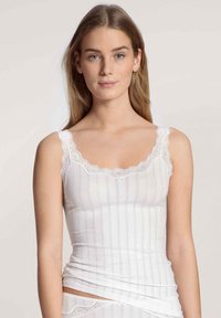 Camisola bianca con pizzo, caratterizzata da righe verticali e una silhouette aderente. Tessuto morbido, spalline regolabili.