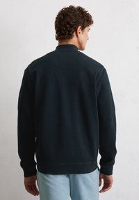 Black pullover sweatshirt with a high neckline, ribbed cuffs, and a textured finish, worn over light blue jeans.