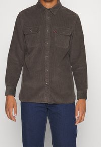 Bruine corduroy overhemd met een knoopsluiting aan de voorkant, twee borstzakken en een kraag. Bevat zilveren knopen en een subtiele ribbelstructuur.