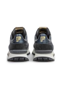 Un par de zapatillas negras y azul marino con suelas blancas, tiradores dorados y logotipos "F" dorados en los talones, mostradas desde la parte trasera sobre un fondo blanco.