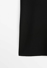 Tissu noir avec un ourlet droit sur un fond blanc uni, montrant la texture et le détail du bord.