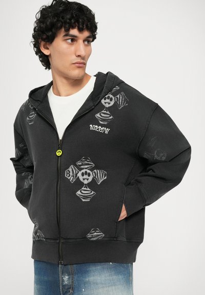 Felpa nera con zip, decorata con motivi grafici di teschi e ossa incrociate. Presenta un cappuccio, tasche frontali e polsini a costine. Tessuto morbido.