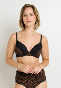 Soutien-gorge noir à motif floral orange, avec des bords festonnés, un soutien-gorge à armatures et un bouton décoratif au centre. Culotte assortie.