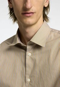 Camicia a righe in beige con sottili righe verticali blu e marroni. Presenta un colletto a punta e due bottoni bianchi.