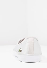 Baskets en cuir blanc à finition lisse, avec un logo crocodile vert brodé sur le talon et une languette arrière en tissu texturé.