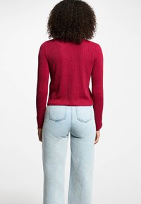 Maglione rigato color marsala con maniche lunghe, design aderente. Abbinato a jeans in denim blu chiaro a vita alta.