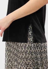 Haut noir à manches courtes avec fentes sur les côtés, associé à une jupe plissée arborant un motif géométrique abstrait en noir et beige.