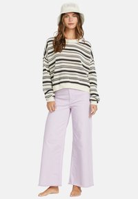 Striped knit sweater in cream and black, paired with wide-leg lavender pants. Model wears a light-colored bucket hat.