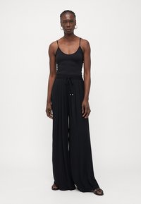 Haut sans manches noir associé à un pantalon large taille haute noir avec un cordon de serrage à la taille et des accents dorés. Texture de tissu lisse.