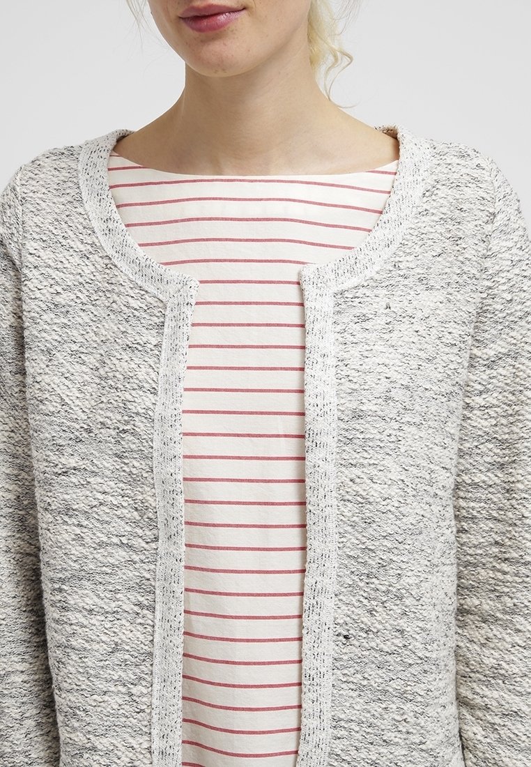 Cardigan texturé gris clair avec encolure ronde, devant ouvert et bordure blanche contrastante ; porté sur un haut à rayures rouges.