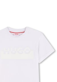 Witte katoenen T-shirt met een ronde halslijn en korte mouwen, voorzien van een groot, lichtgekleurde "HUGO" logo op de borst. Rode label binnenin.