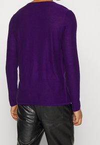 Långärmad lila tröja med rund halsringning, figurnära design och mjuk textur, kombinerad med svarta läderbyxor.