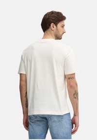 Camiseta de algodón crema con mangas cortas, cuello redondo y un corte holgado. Textura ligera, combinada con jeans de mezclilla azul claro.
