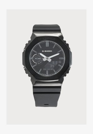 Montre-bracelet noire G-Shock avec affichages analogique et numérique, bracelet texturé, indicateur de jour et aiguilles argentées des heures et des minutes sur fond gris.