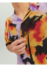 Camisa de botones de manga corta con un patrón multicolor y estampados de palmeras, en tonos de púrpura, naranja y negro, hecha de una tela ligera.