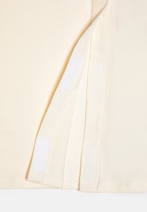 Tessuto color crema con chiusure a velcro su un lato, che mostra una texture liscia e dettagli di cucitura pulita.