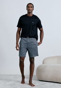 Μαύρο βαμβακερό t-shirt με στρογγυλή λαιμόκοψη και μικρό λογότυπο· γκρι σορτς με γεωμετρικό μαύρο σχέδιο και ελαστική μέση. Σύνολο καθημερινής άνετης ένδυσης.