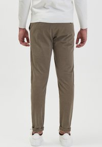 Bruine ribfluwelen broeken met een geribbelde textuur, met een slim fit en opgerolde zoom, gecombineerd met witte sneakers en een witte trui.