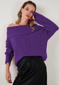 Maglione off-the-shoulder in maglia purpurea strutturata. Design crop con motivo a coste; si abbina a una gonna in satin nero liscio.