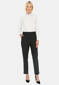 Biała koszula z guzikami i czarne strukturalne spodnie o dopasowanym kroju. Stylizacja dopełniona jest czarnymi szpilkami i prostymi liniami.