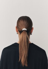 Pferdeschwanz, gehalten von einer silbernen Haarspange mit mehreren schimmernden Strasssteinen, vor einem Hintergrund aus langem, glattem braunem Haar.