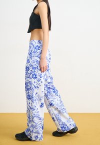 Vidje byxor i blått och vitt blommönster, tillverkade av texturerad tyg. Kombineras med en åtsittande svart croptop och svarta skor.