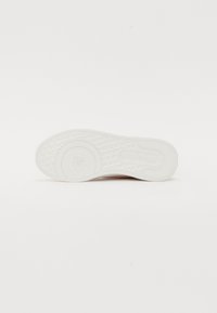 White sneaker sole with a textured pattern and circular logo; smooth rubber material, rounded shape, and subtle branding detail.