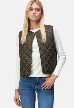 Gilet matelassé vert olive avec des boutons-pression, porté par-dessus une chemise blanche à manches longues, associé à un jean bleu. Matériau lisse et léger.